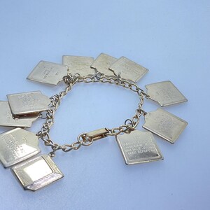 May include: A gold-toned charm bracelet with multiple rectangular and diamond-shaped charms. The charms are connected by a chain and clasp. Some charms have visible text. The bracelet is displayed on a light background.