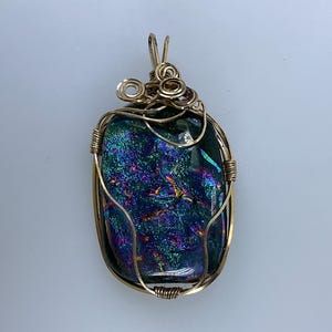 May include: A gold wire wrapped pendant featuring a dichroic glass stone with iridescent blue, green, and purple hues.