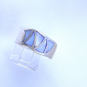 May include: A silver ring with a geometric design. The ring features a series of light blue, triangular inlays set within a silver band. The ring is displayed on a clear, plastic ring holder against a white background.