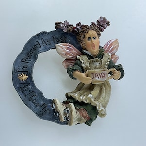 May include: A whimsical fairy figurine with pink wings, brown hair, and a green dress, holding a coffee cup that says "JAVA". The fairy is on roller skates and has a banner that says "I'm Running As Fast As I Can!"