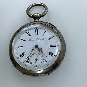 May include: Silver pocket watch with Roman numeral markings on the face. The watch face reads "Niagara Watch Co."
