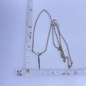 K&ouml;nnte beinhalten: Silberfarbene Halskette mit einem Anh&auml;nger, der eine Figur mit ausgestreckten Armen darstellt. Die Kette ist filigran. Die Halskette ist etwa 5 cm lang, wie auf dem Lineal im Bild angegeben.