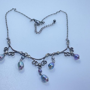 May include: A silver-toned necklace with a delicate design. The necklace features small clear crystals and iridescent, teardrop-shaped pearls. The chain is adjustable. A beautiful piece of jewelry.