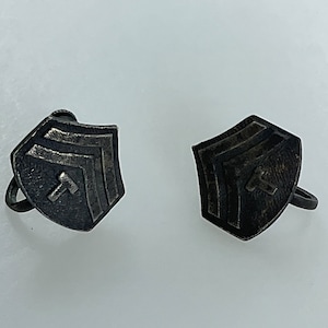 May include: A pair of silver cufflinks with a geometric design. Each cufflink features a shield shape with a series of three chevron shapes and a small arrow in the center.