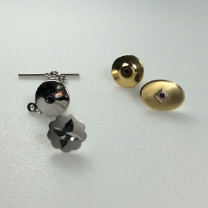 May include: Three silver and gold tie tacks. One silver tie tack has a chain and a bar. Another silver tie tack has a star design. The gold tie tack has a red stone in the center.