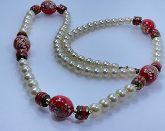 May include: A vintage pearl necklace with red and floral-decorated beads. The necklace features multiple strands of faux pearls, interspersed with red, gold, and brown accent beads. The necklace is a classic piece of jewelry.