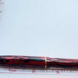 May include: A red and black striped fountain pen with a gold band, measuring approximately 4 inches in length.