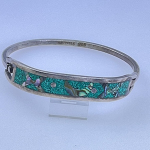May include: A silver hinged bracelet with a turquoise and abalone inlay. The bracelet is marked "925 Sterling". The turquoise inlay is a mosaic design, and the abalone pieces have iridescent colors. The bracelet is a piece of jewelry.