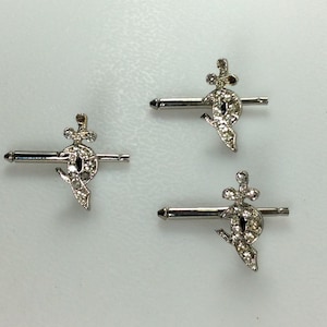 May include: Three silver cufflinks with a jeweled design. Each cufflink features a small, round, black stone surrounded by smaller, clear stones. The stones are set in a silver design that resembles a stylized sword.