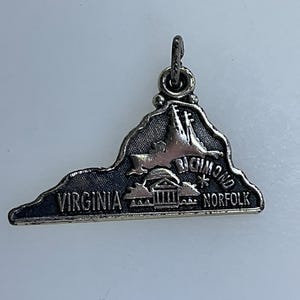 May include: Silver charm shaped like the state of Virginia, with the cities of Richmond and Norfolk labeled. The charm has a loop at the top for attaching to a necklace or bracelet.