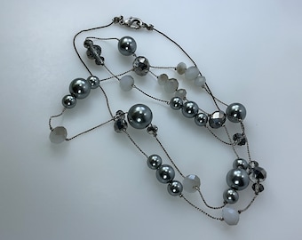 Può includere: Una collana multifilo con catena argentata e perline grigie e bianche.
