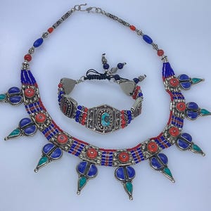 May include: A silver necklace with blue and red beads and turquoise accents. The necklace has a pendant with a large turquoise stone. The necklace is paired with a matching bracelet.