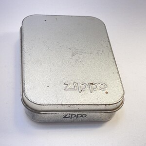 Puede incluir: Una caja met&aacute;lica rectangular de color plateado con bordes redondeados. La palabra "Zippo" est&aacute; grabada en la tapa y en la parte inferior de la caja. La caja tiene un aspecto ligeramente desgastado.