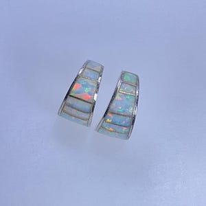 May include: A pair of silver hoop earrings with inlaid opal stones. The earrings have a curved, geometric design with rectangular opal segments. The opals display iridescent colors of blue, green, and red.