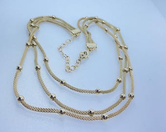 May include: A gold-toned necklace with three strands. Each strand is made of a fine mesh chain and interspersed with small, round beads. The necklace has a lobster clasp and an adjustable chain for sizing.