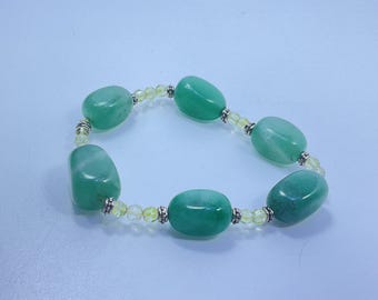 May include: A green gemstone bracelet featuring large, oval-shaped beads. The bracelet is strung with smaller yellow beads and silver-colored spacers. The gemstones have a polished, smooth surface, and the bracelet is displayed on a light blue background.