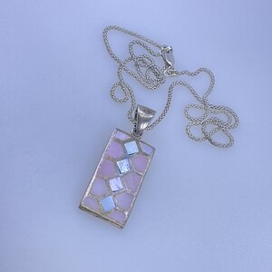 May include: A silver necklace with a rectangular pendant. The pendant features a mosaic design of pink and iridescent squares. The chain is a delicate silver link. The necklace is displayed on a white surface.