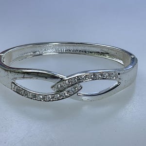 May include: A silver bangle bracelet with a delicate, intertwined design accented with clear rhinestones.