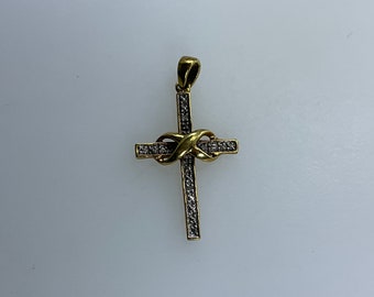 May include: A gold cross pendant with a diamond-encrusted design. The cross features a knot design in the center.