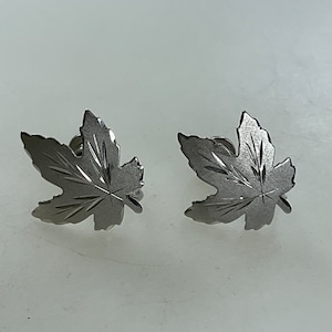 May include: A pair of silver maple leaf earrings. The leaves are detailed with etched lines.