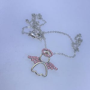 May include: A silver-colored necklace with a pendant shaped like an angel. The angel pendant has pink crystal accents on the wings and halo. The necklace chain is delicate and has a lobster clasp.