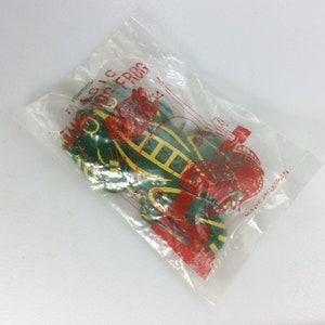 May include: A green and yellow toy frog in a clear plastic bag with red lettering that says "Magic Frog" and "Made in Japan".