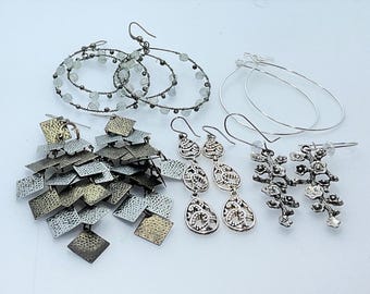 Può includere: Un set di cinque paia di orecchini. Gli orecchini sono realizzati in argento, oro e perline trasparenti. Gli orecchini sono tutti di stili diversi, tra cui orecchini a cerchio, orecchini pendenti e orecchini a bottone.