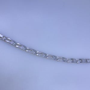 May include: A silver-colored bracelet with a rectangular link design. The bracelet is made of metal and has a polished finish. The links are connected in a repeating pattern. The bracelet is shown on a light blue background.