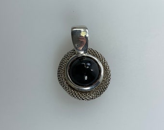 May include: A silver pendant with a black gemstone set in a circular silver frame. The frame is made of a woven chain design.
