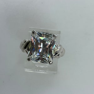 May include: A silver ring with a large, clear square-shaped cubic zirconia stone.