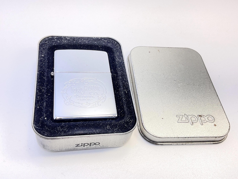 Puede incluir: Un encendedor Zippo plateado con un dise&ntilde;o grabado, presentado en una caja de metal. El encendedor presenta el texto "Terra Mater" y otras letras. La caja est&aacute; abierta, revelando el encendedor en terciopelo negro.