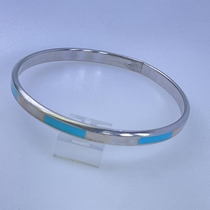 May include: A silver bangle bracelet with rectangular turquoise inlays. The bracelet is round and has a polished finish. The turquoise inlays are evenly spaced around the bracelet. A simple, elegant piece of jewelry.