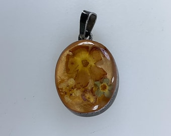 May include: A silver pendant with a clear oval resin charm containing pressed dried flowers in shades of yellow, orange, and green.