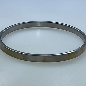 May include: A silver bangle bracelet with a white and gold inlay.