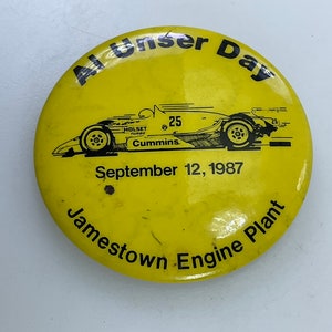 May include: Yellow round button with black text and a black and white illustration of a race car. The text reads "Al Unser Day", "September 12, 1987", and "Jamestown Engine Plant".