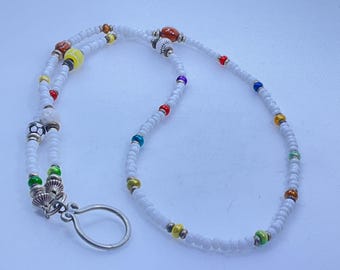 May include: White beaded lanyard with colorful accent beads. The lanyard features a variety of beads in red, yellow, green, blue, and brown. A silver-colored clasp is attached at the bottom.
