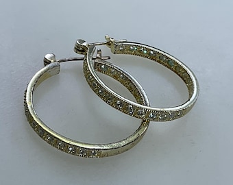 May include: A pair of silver hoop earrings with a row of clear rhinestones around the edge.