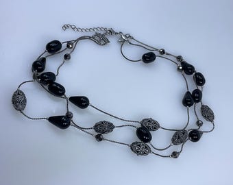 May include: A three-strand necklace with black beads and silver accents. The necklace features a silver clasp and a variety of black beads, including round and teardrop shapes.