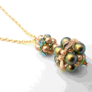Op de afbeelding: Een gouden ketting met een hanger gemaakt van groene en gouden kralen. De hanger is een cluster van kleine kralen in een bolvorm.