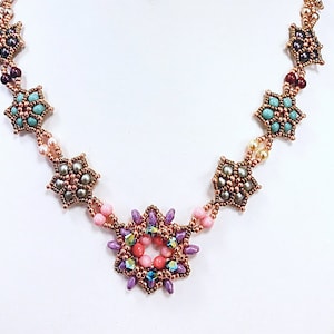 Op de afbeelding: Een kralenketting met een stervormig ontwerp in tinten roze, paars, turquoise en bruin. De ketting heeft een grote, centrale stervormige hanger.
