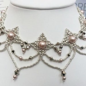 May include: A silver and blush pink beaded necklace with a delicate, intricate design. The necklace features a central motif of three star-shaped clusters of beads, each with a larger blush pink pearl in the centre. The necklace is accented with smaller silver beads and has a cascading effect with multiple strands of beads.
