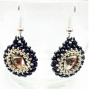 Może przedstawiać: Para srebrnych kolczyków wiszących z czarnymi i srebrnymi koralikami i przezroczystym kryształem w środku.