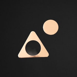 May include: A gold triangle with a circle cut out of the center, and a smaller gold circle above it, both on a black background.