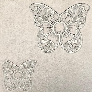May include: Two gray butterfly designs with floral patterns. The larger butterfly has a detailed floral center and wing designs. The smaller butterfly mirrors the larger one, both set against a textured gray background. The designs are embossed.