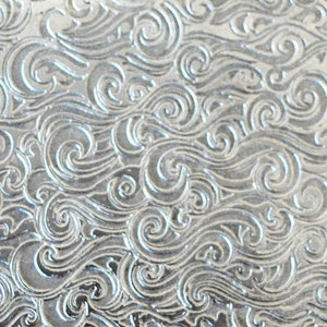 May include: Close-up of two metal surfaces with a swirling pattern. The surface on the left is copper and the surface on the right is silver.