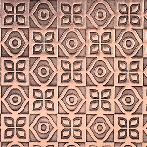 May include: A detailed, repeating pattern in shades of copper and brown. The design features a symmetrical arrangement of floral and geometric shapes, creating a textured, decorative surface. The pattern is consistent across the entire rectangular surface.