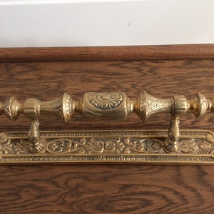 Może przedstawiać: Złoty klamka do drzwi z ozdobnym wzorem. Klamka jest przymocowana do prostokątnej płytki z podobnym wzorem.