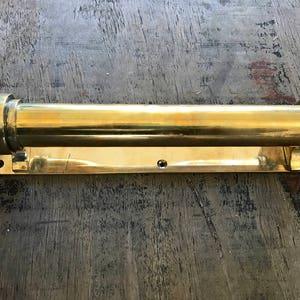 May include: A brass towel bar with a cylindrical design and a rectangular base. The bar is mounted on a wall.