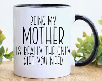 May include: White ceramic coffee mug with a black rim and handle. The mug has black text that reads "Being my Mother is really the only gift you need."