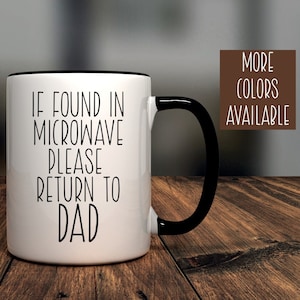 May include: White ceramic coffee mug with a black rim and handle. The mug has black text that reads "If found in microwave please return to dad."